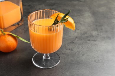 Photo of Delicious tangerine liqueur in glass and fresh fruits on grey table, closeup. Space for text