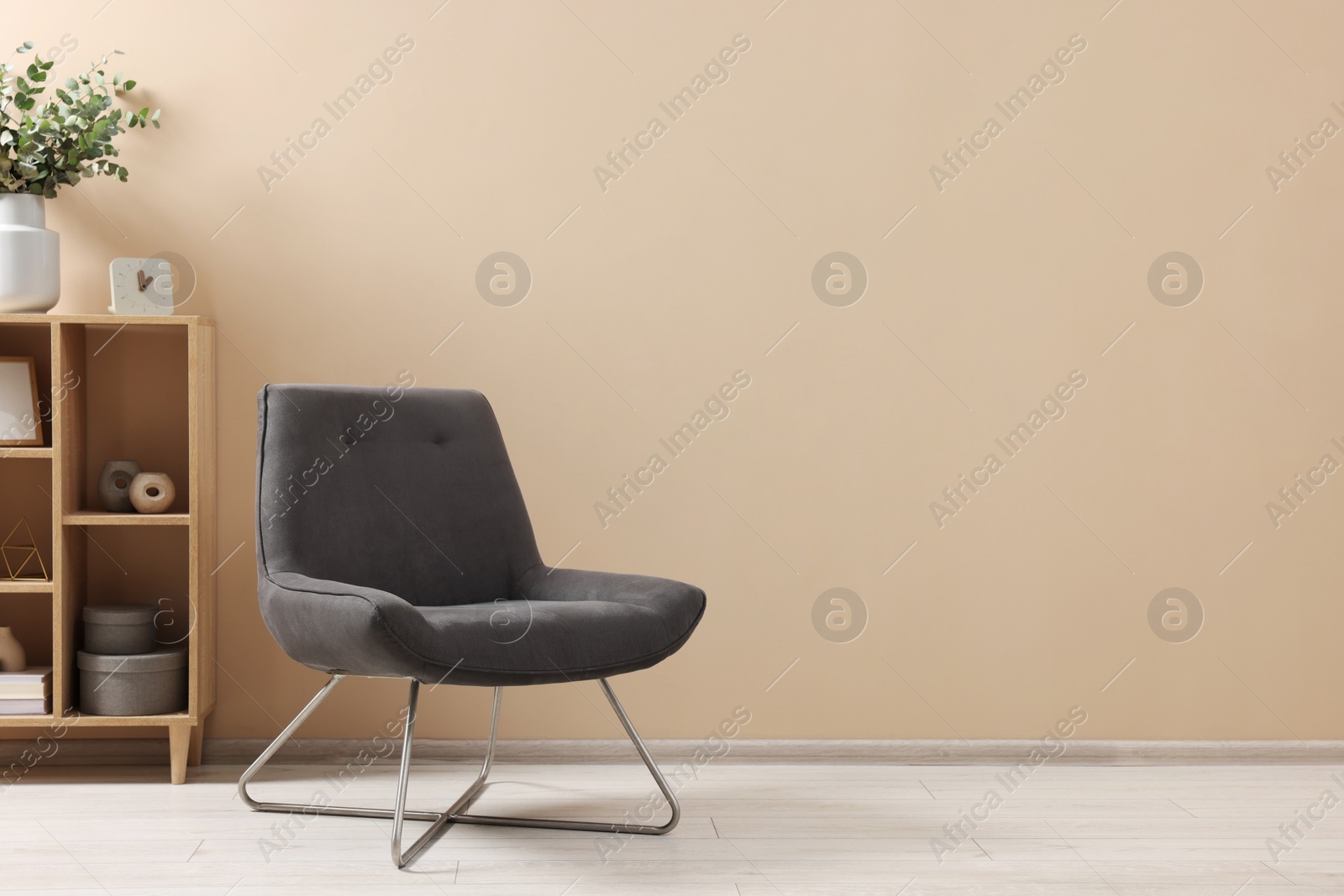 Photo of Living room interior with comfortable armchair and shelving unit near beige wall indoors. Space for text