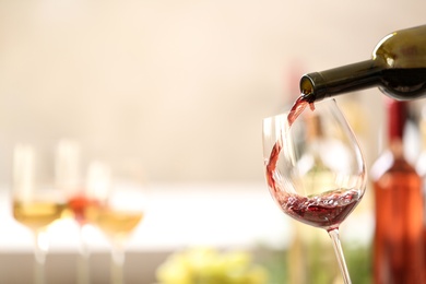 Photo of Pouring red wine from bottle into glass on blurred background. Space for text