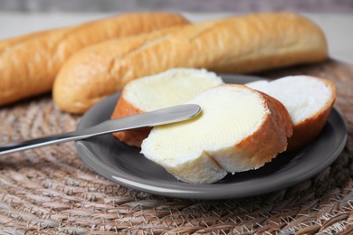 Photo of Cut baguette with fresh butter on wicker mat, closeup