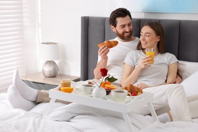 Photo of Happy couple eating tasty breakfast on bed at home