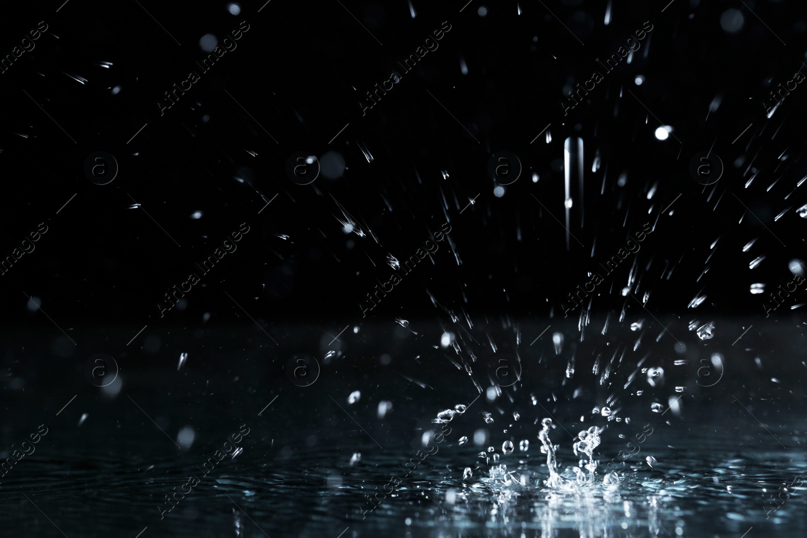 Photo of Rain drop falling down into puddle on dark background