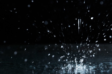 Photo of Rain drop falling down into puddle on dark background