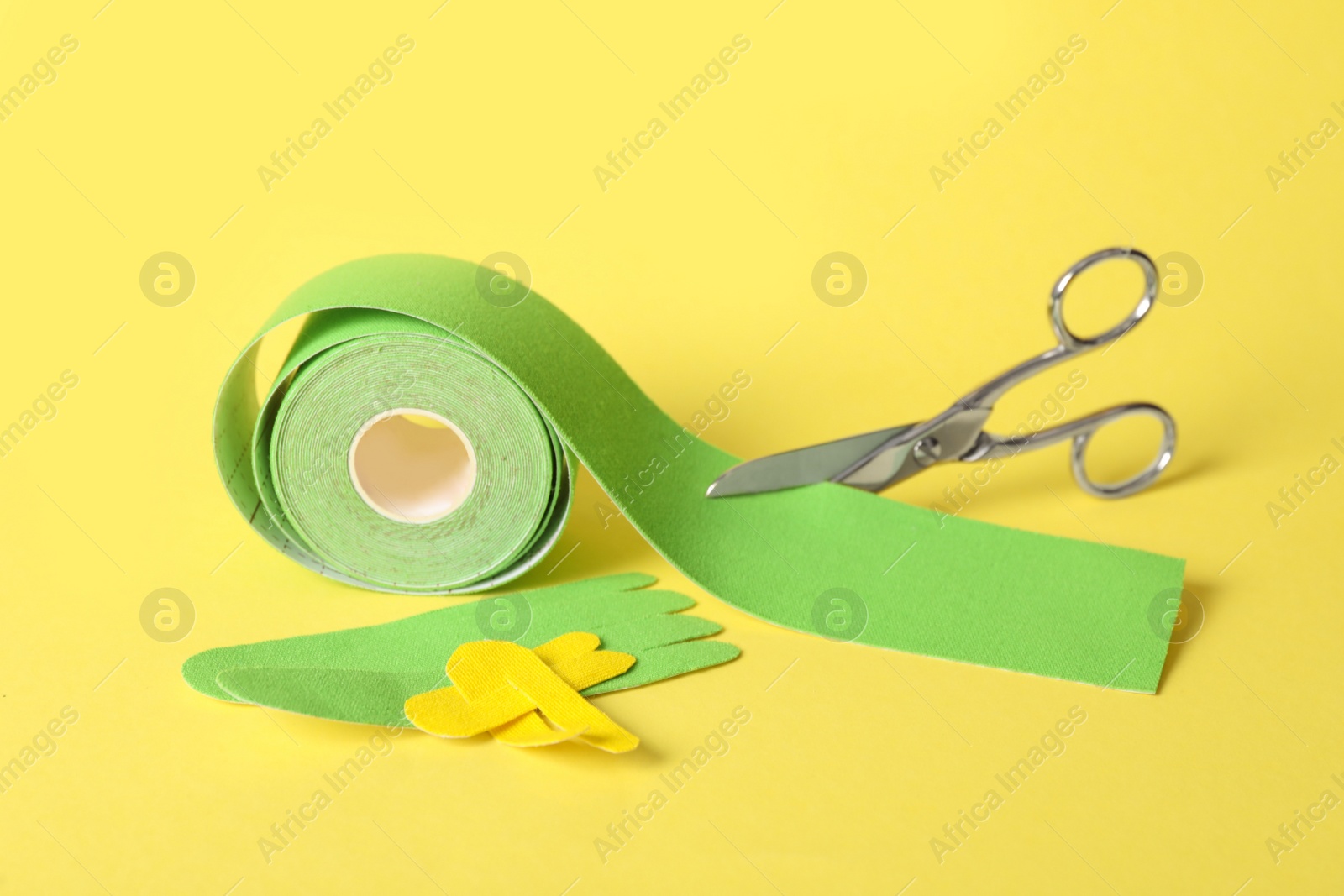 Photo of Scissors, bright kinesio tape roll and pieces on yellow background