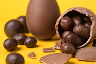 Photo of Tasty whole and broken chocolate eggs with candies on yellow background, closeup