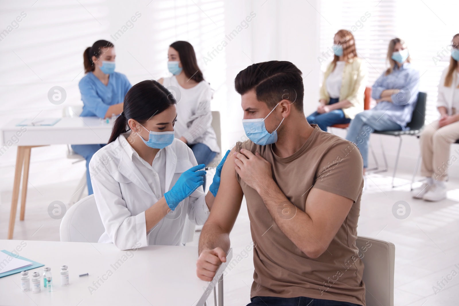 Photo of Doctor giving injection to patient while other waiting in line at hospital. Vaccination campaign