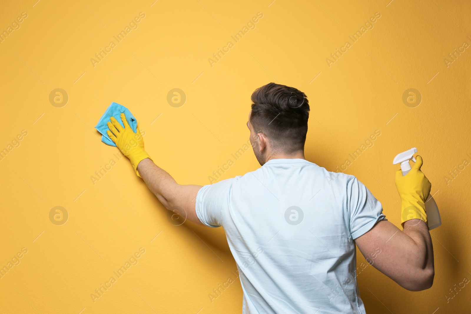 Photo of Man cleaning color wall with rag and sprayer