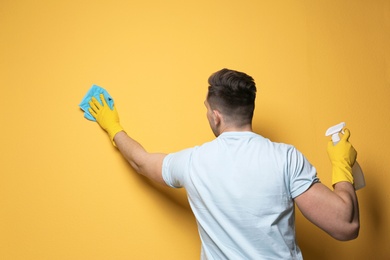 Photo of Man cleaning color wall with rag and sprayer