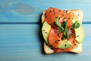 Photo of Tasty toast with butter, salmon, avocado, sesame seeds and microgreens on light blue wooden table, top view. Space for text