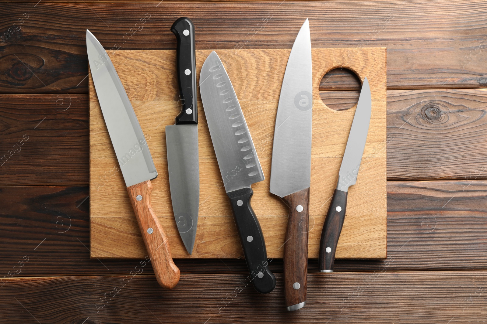 Photo of Many different knives and board on wooden table, top view