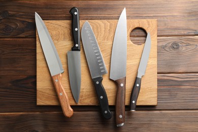 Photo of Many different knives and board on wooden table, top view