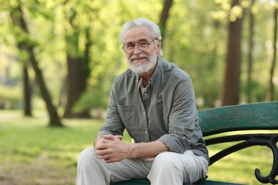 Portrait of happy grandpa with glasses on bench in park