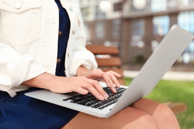 Photo of Woman using laptop on bench outdoors, closeup