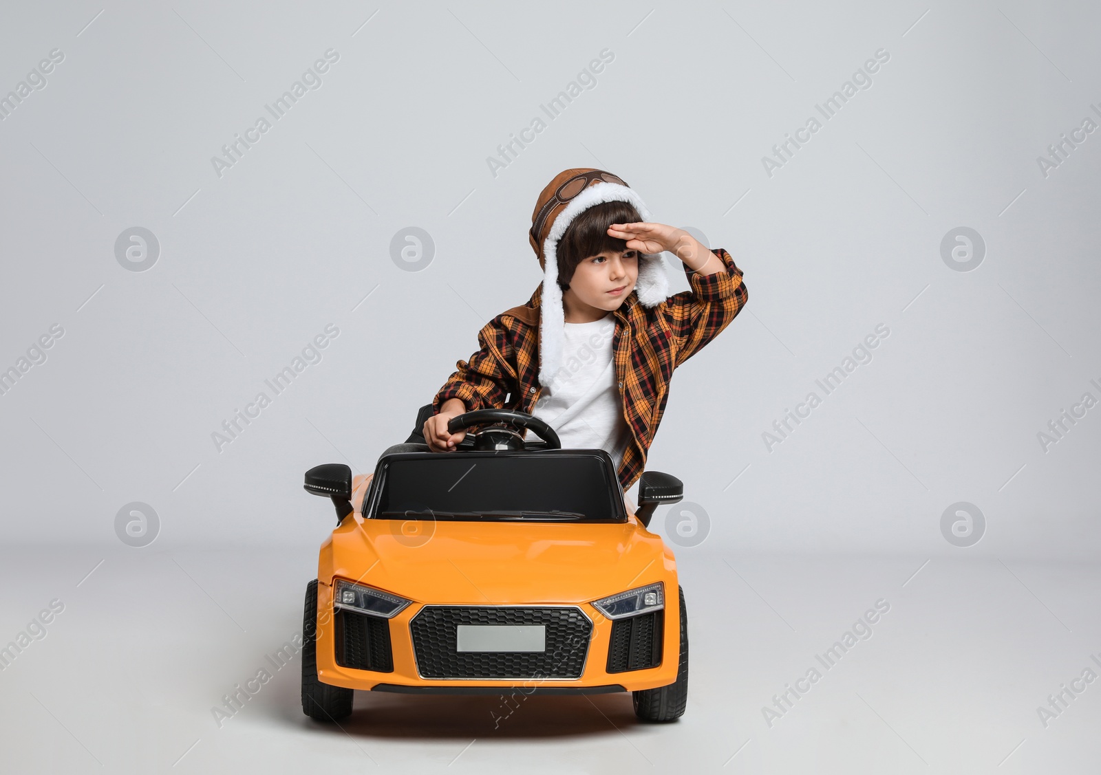 Photo of Cute little boy in pilot hat driving children's electric toy car on grey background