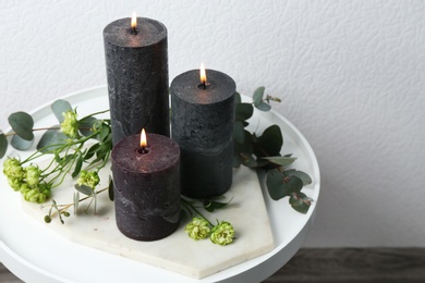 Photo of Set of burning candles, flowers and green branches on table at white wall, space for text