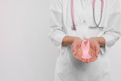 Doctor with stethoscope holding pink ribbon on white background, closeup and space for text. Breast cancer awareness