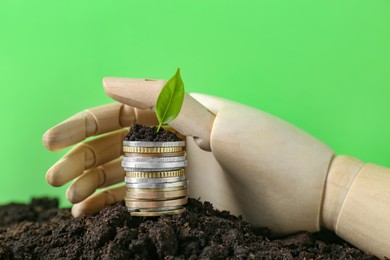 Photo of Stack of coins, green plant and wooden mannequin hand on soil against blurred background. Profit concept