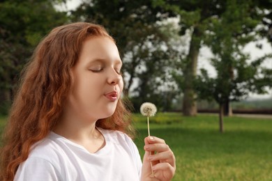 Photo of Cute girl with beautiful red hair blowing dandelion in park, space for text. Allergy free concept