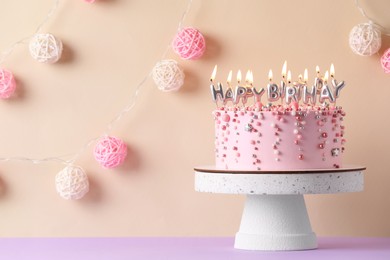 Photo of Birthday cake with burning candles on violet table, space for text