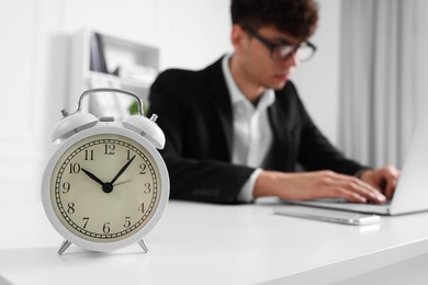 Photo of Man working at white table in office, focus on alarm clock. Deadline concept