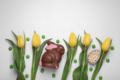 Flat lay composition with chocolate bunny, tulips and candies on white background, space for text. Easter celebration