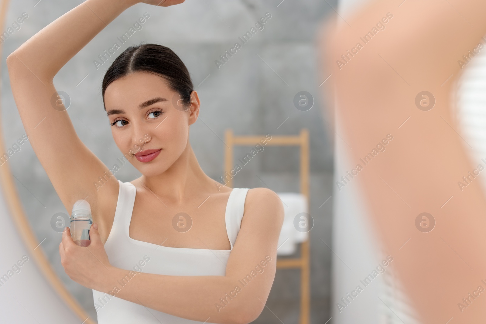 Photo of Beautiful woman applying deodorant near mirror in bathroom