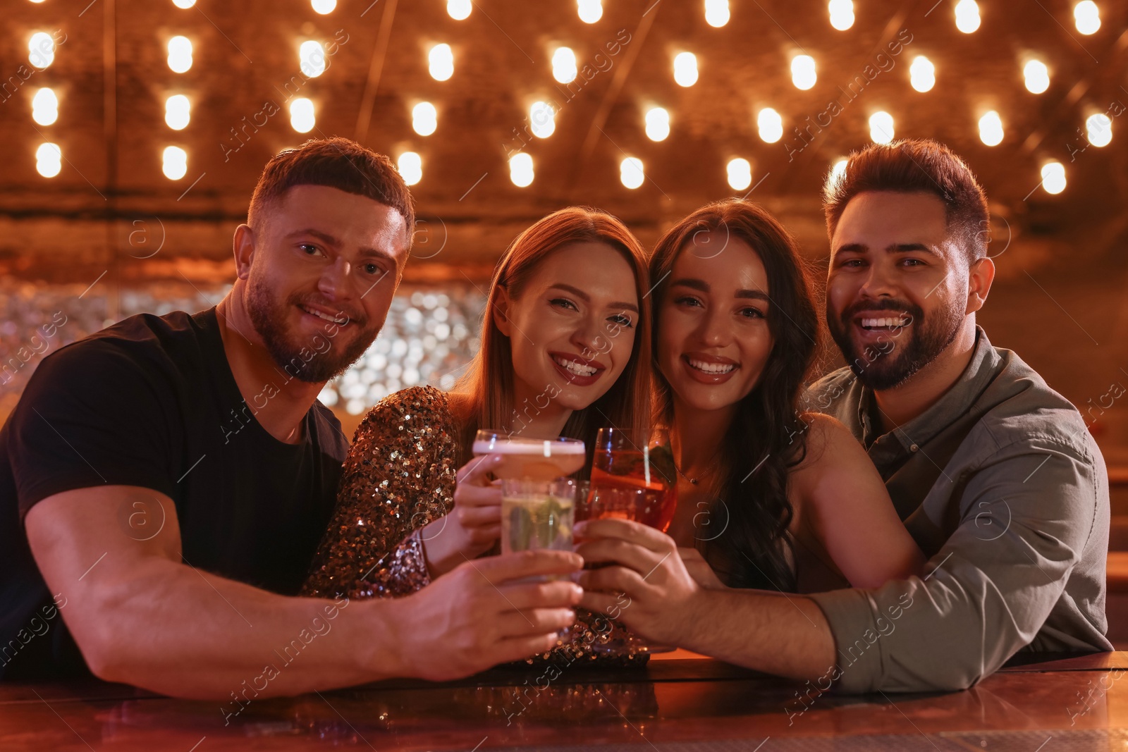 Photo of Happy friends clinking glasses with fresh cocktails in bar