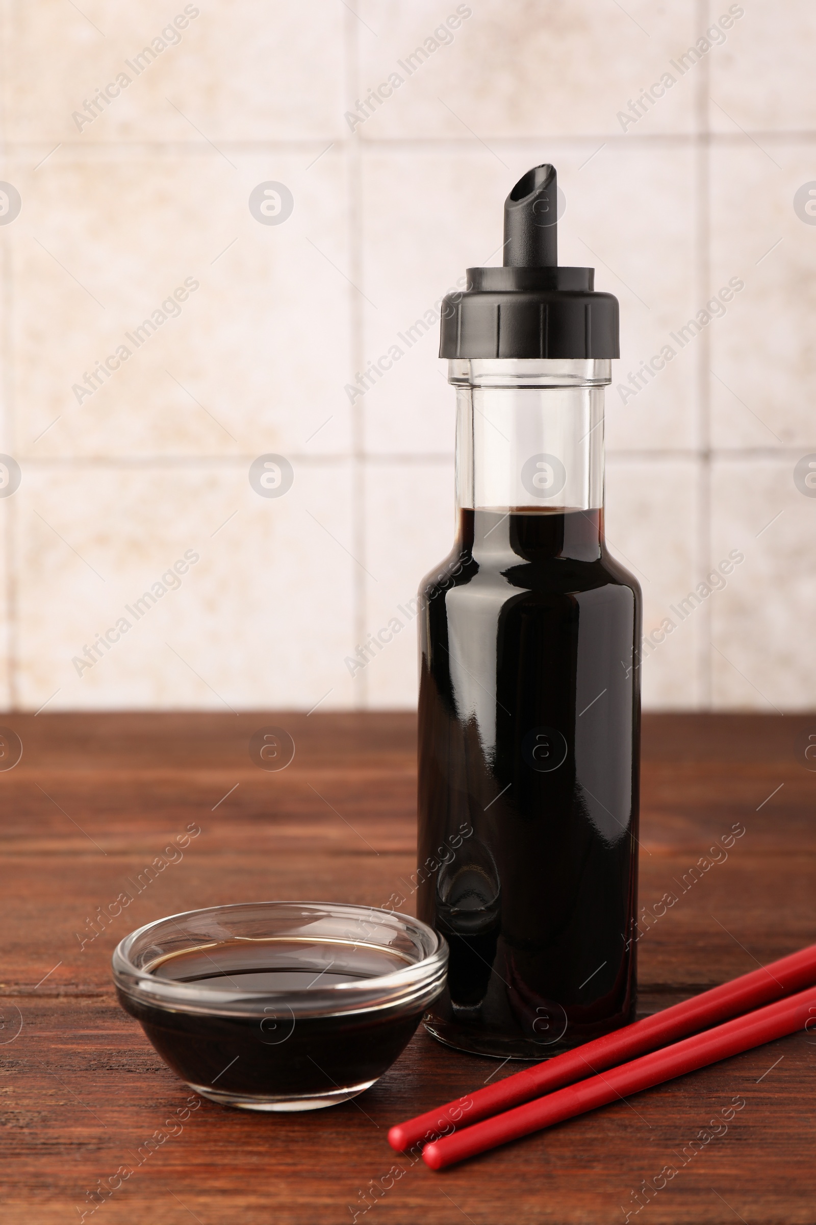 Photo of Bottle, bowl with soy sauce and chopsticks on wooden table