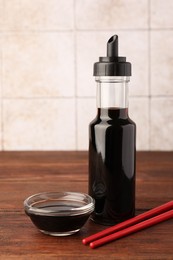 Photo of Bottle, bowl with soy sauce and chopsticks on wooden table