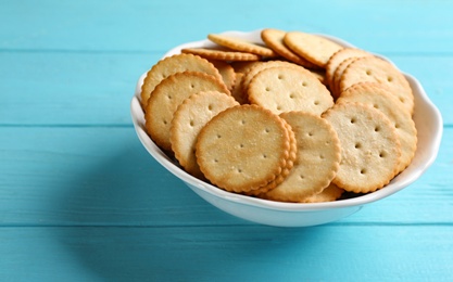 Photo of Delicious crispy crackers in bowl on turquoise wooden table