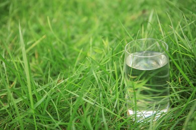 Photo of Glass of fresh water on green grass outdoors, space for text