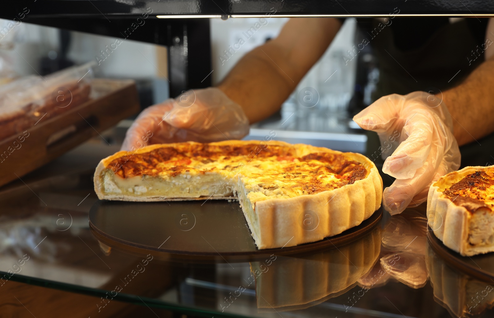 Photo of Seller taking tasty quiche from showcase in bakery shop, closeup