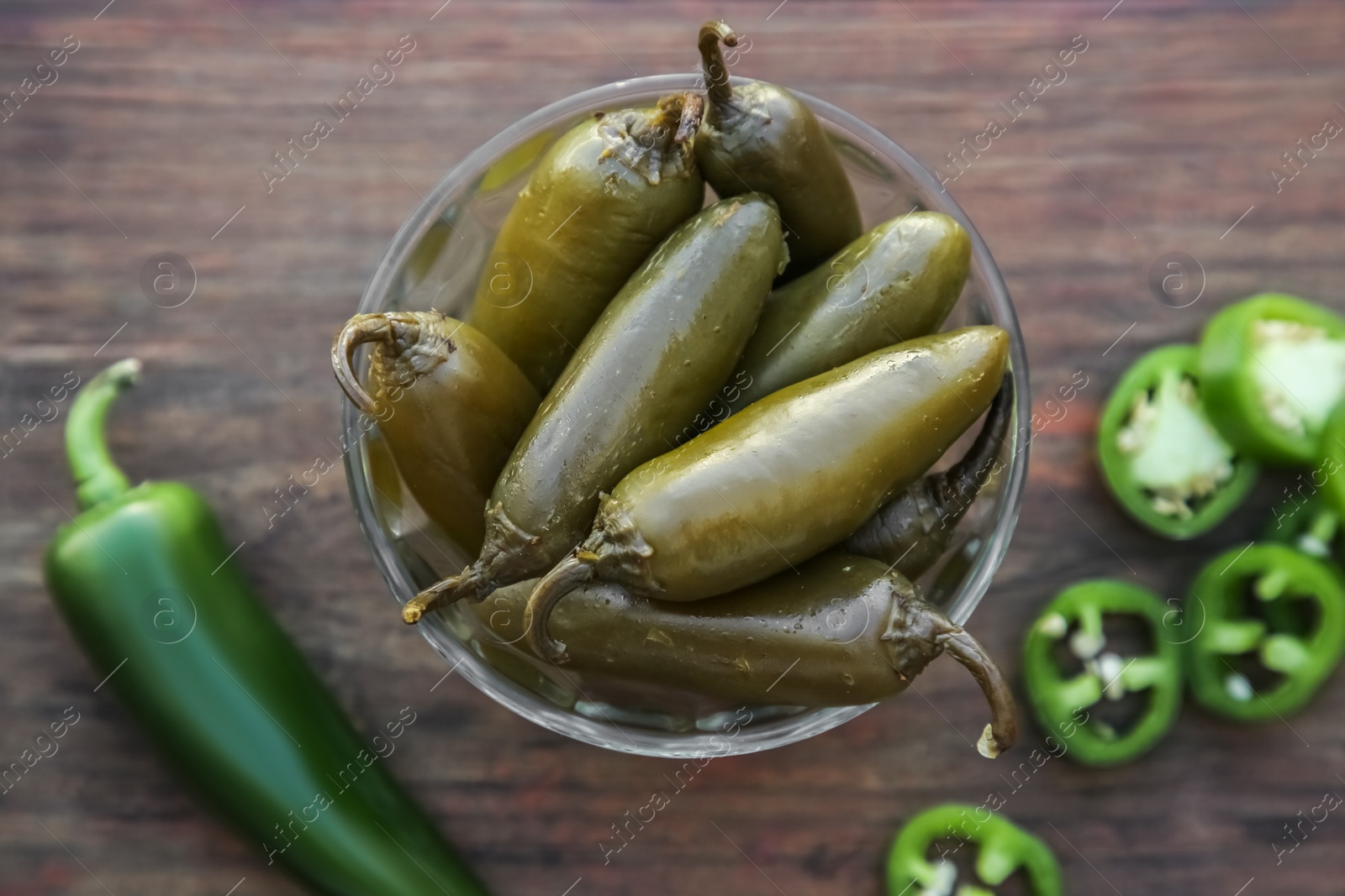 Photo of Fresh and pickled green jalapeno peppers on wooden table, flat lay