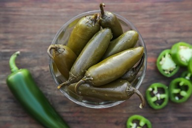 Fresh and pickled green jalapeno peppers on wooden table, flat lay