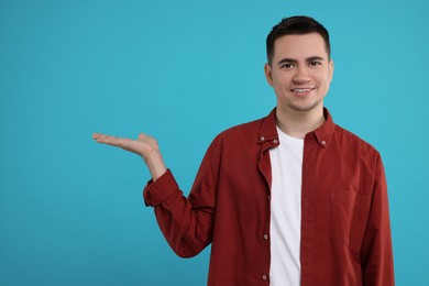 Photo of Special promotion. Happy man showing something on light blue background, space for text