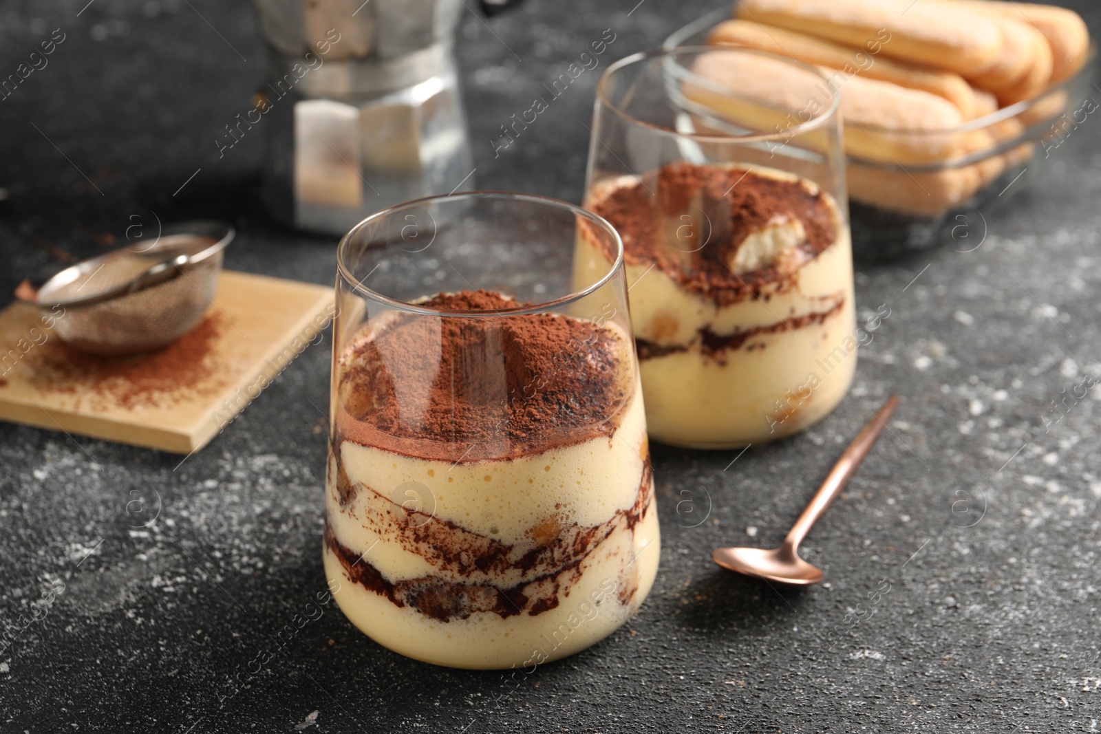 Photo of Delicious tiramisu in glasses on grey textured table, closeup