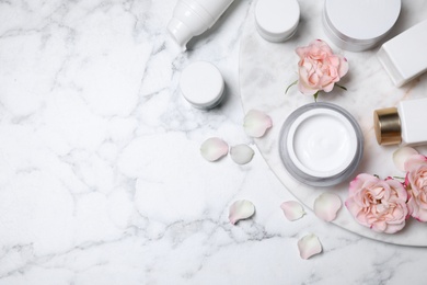 Flat lay composition with different skin care products and flowers on white marble background, space for text