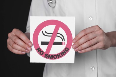 Photo of Doctor holding card with no smoking sign on black background, closeup