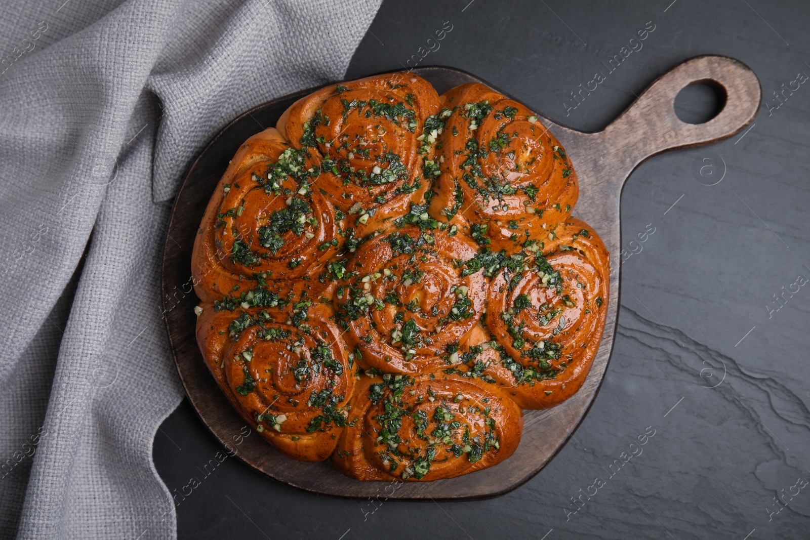 Photo of Traditional Ukrainian garlic bread with herbs (Pampushky) on black table, flat lay