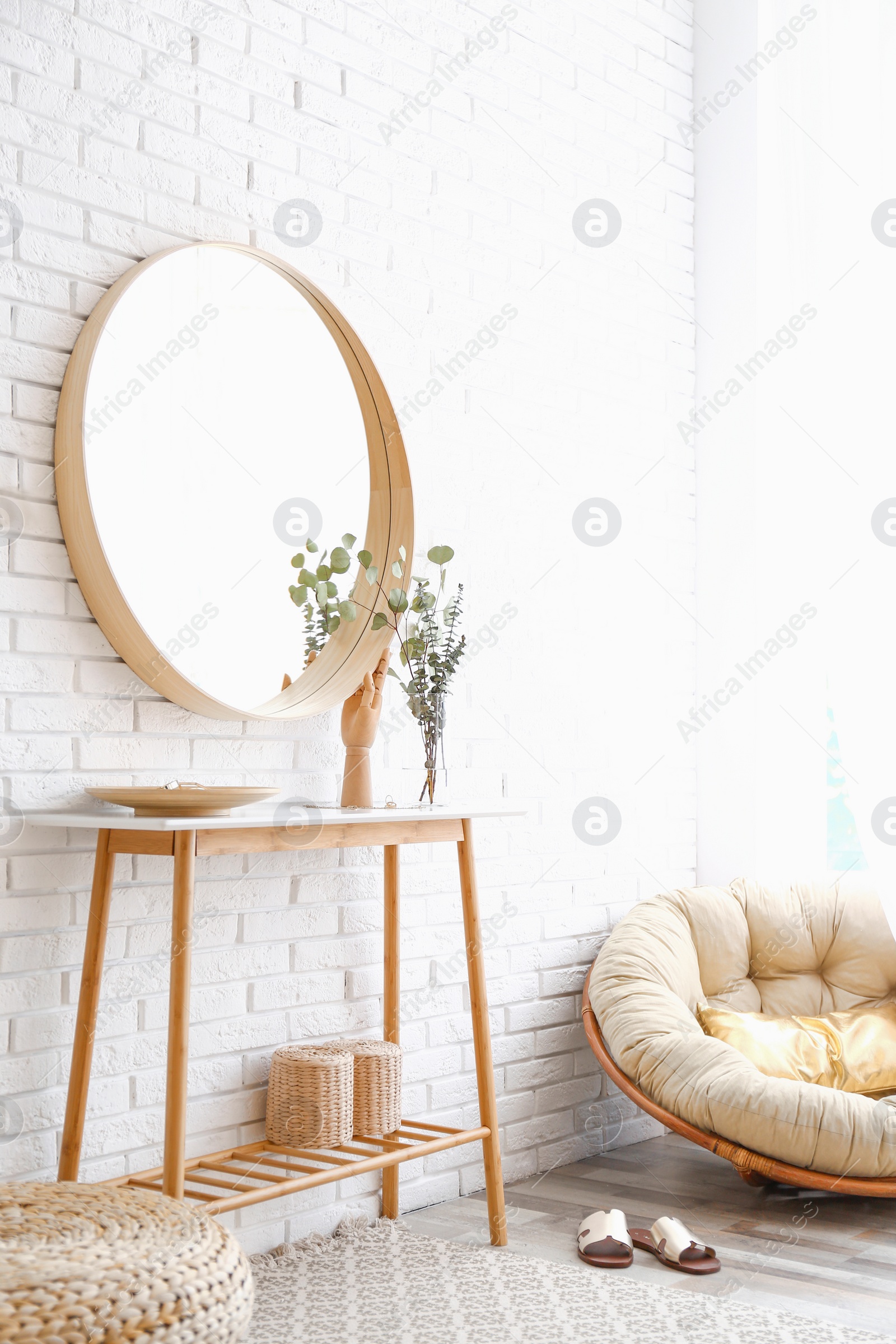 Photo of Hallway interior with big round mirror, table and decor near brick wall