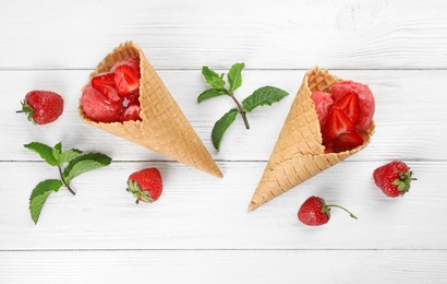 Photo of Delicious strawberry ice cream in wafer cones on white wooden table, flat lay
