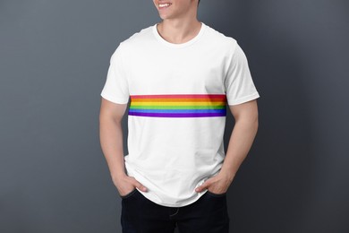 Young man wearing white t-shirt with image of LGBT pride flag on grey background