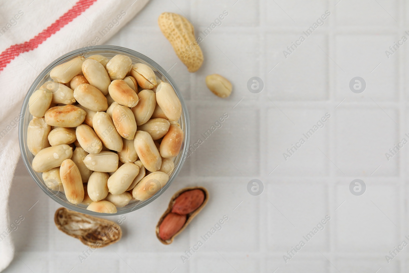 Photo of Roasted peanuts in bowl on white tiled table, top view. Space for text