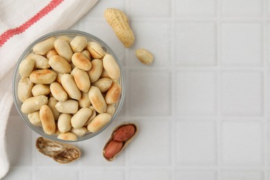 Photo of Roasted peanuts in bowl on white tiled table, top view. Space for text