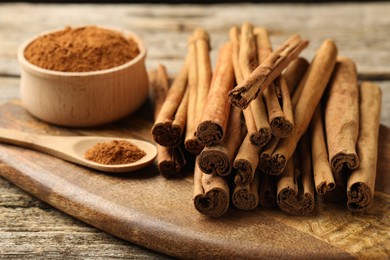 Photo of Cinnamon powder and sticks on wooden table, closeup