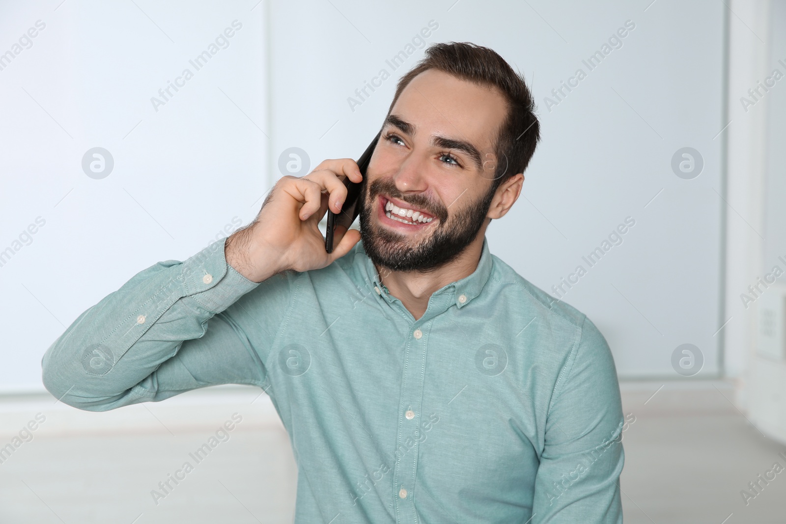 Photo of Young man laughing while talking on phone indoors