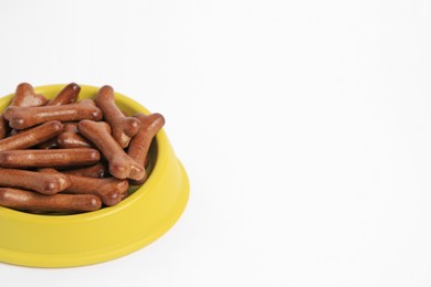 Photo of Yellow bowl with bone shaped dog cookies on white background. Space for text
