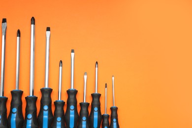 Photo of Set of screwdrivers on orange background, flat lay. Space for text