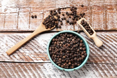 Photo of Aromatic spice. Black pepper in bowl, spoon and scoop on wooden table, flat lay