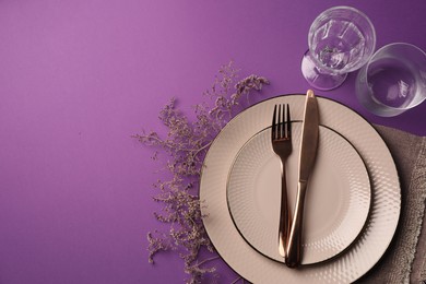 Stylish table setting. Plates, cutlery, glasses and floral decor on purple background, flat lay with space for text